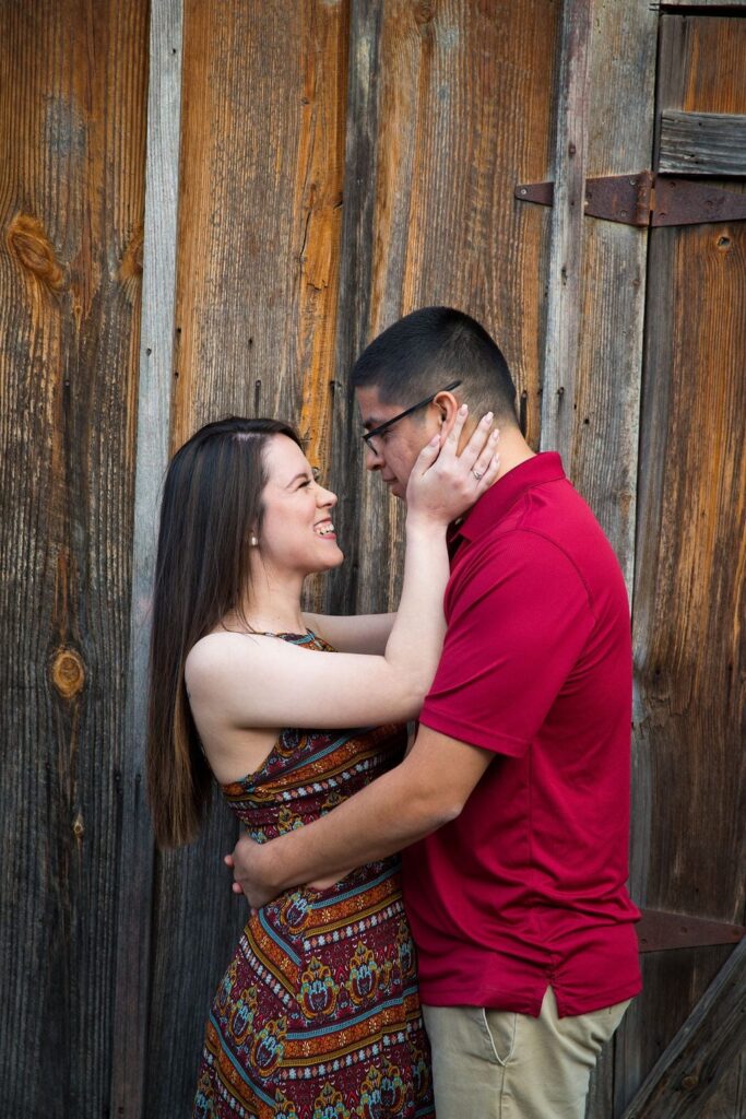Aamber and Alex engagement session in Gruene Tx on wooden wall looking at each other