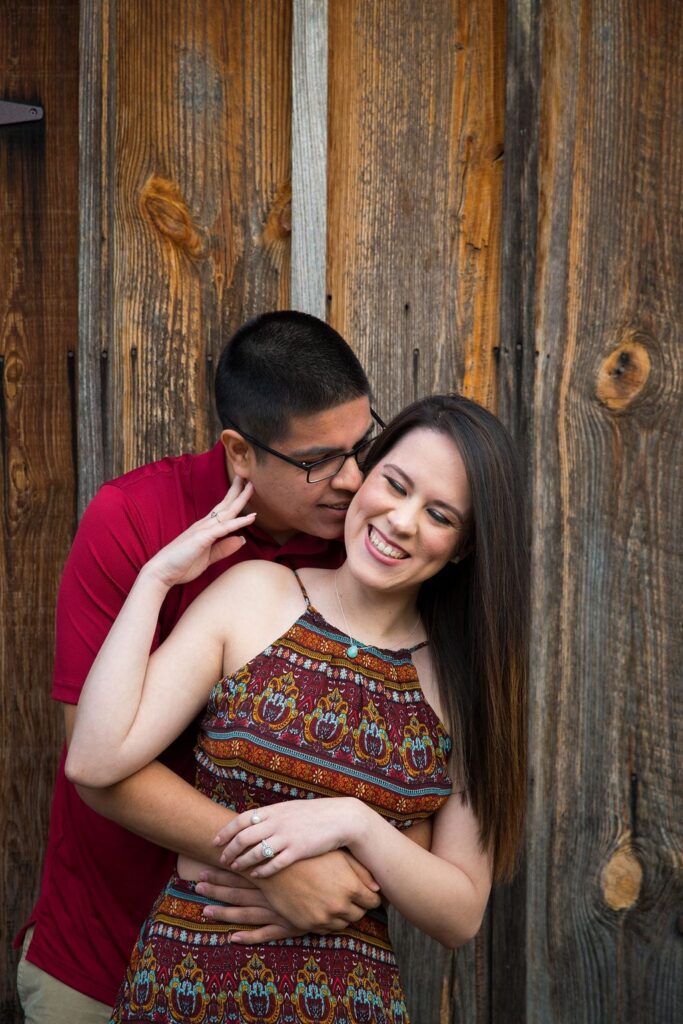 Aamber and Alex engagement session in Gruene Tx on wooden wall kissing red