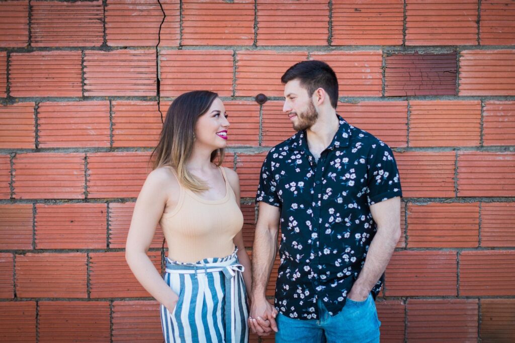 Liz and Ruben engagement looking at each other on red brick wall downtown New Braunfels