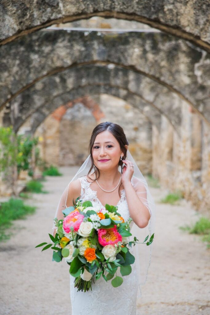 Gaby Bridal at Mission San Jose in arches holding flowers