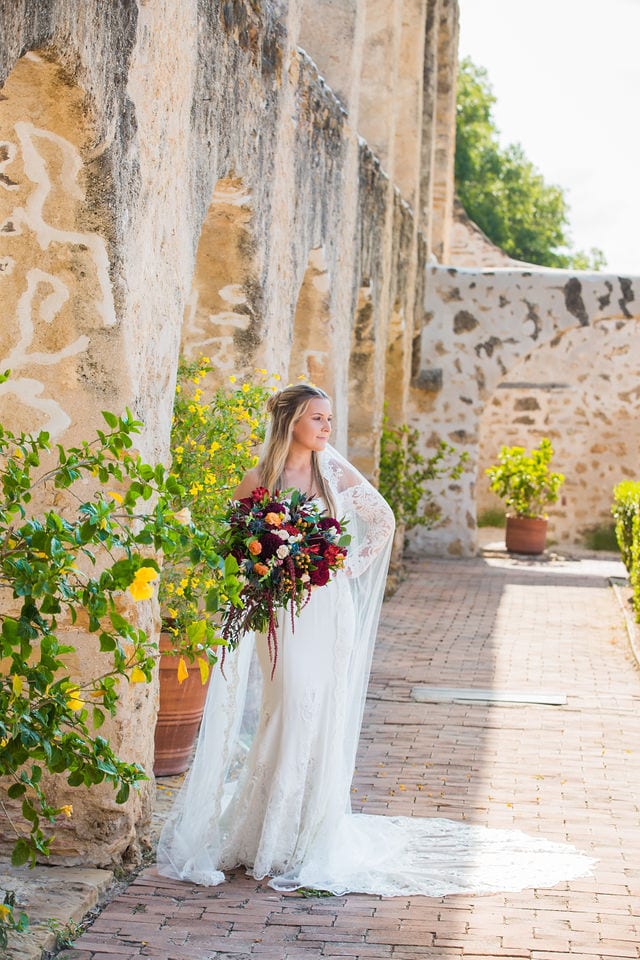 Kelsey's bridal at Mission San Jose outside arches with bouquet looking out
