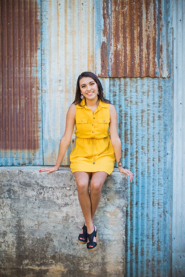 Aubree's Senior session in Gruene sitting by rusted wall