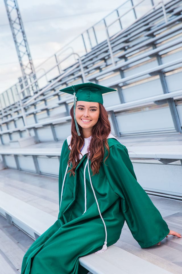 Faith Senior session in Marion cap and gown on sitting on bleachers