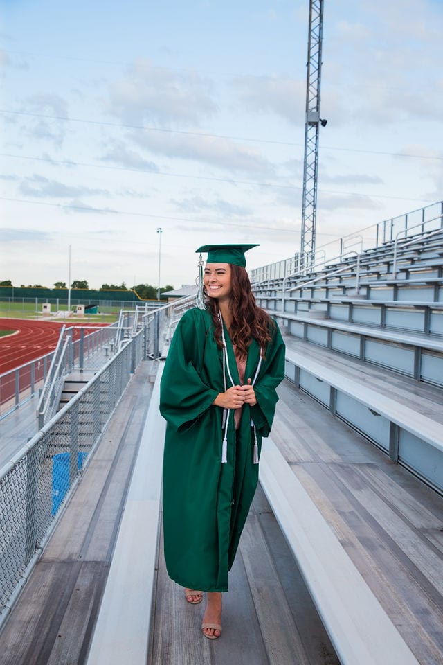 Faith Senior session in Marion cap and gown walking on bleachers