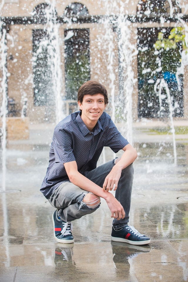 Wyatt's senior session the Pearl kneeling by water feature