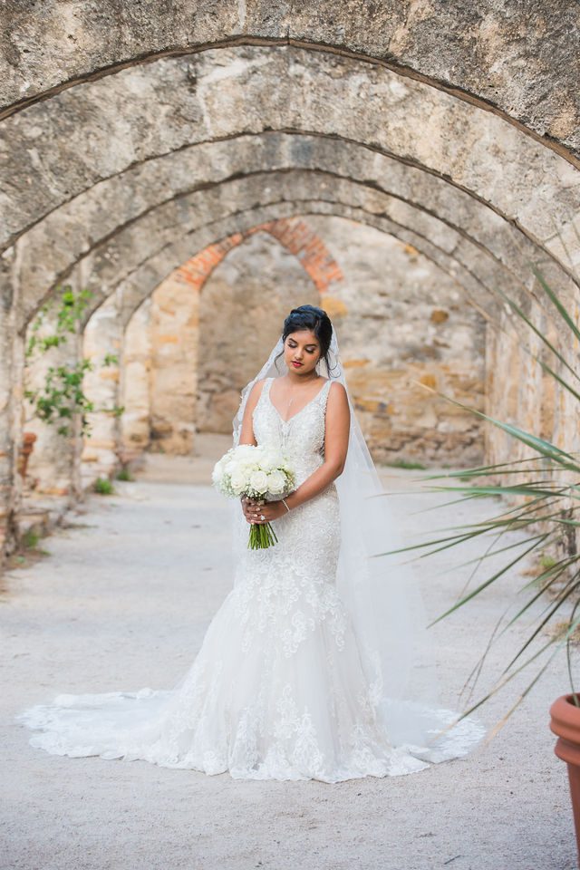 Sonali's bridal portrait in the arches of Mission San Jose looking at bouquet