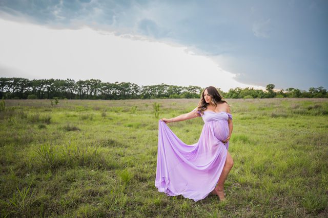 Yoli maternity session at Cibolo Natural Area mom in the grass holding the dress